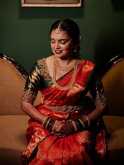 A beautiful portrait of a bride in a traditional red and green saree, seated in one of our heritage rooms.