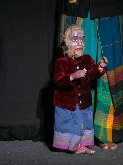 An elder character, portrayed by a string puppet from the Sri Lankan performance. The detailed carving and costume convey a sense of wisdom and history.
