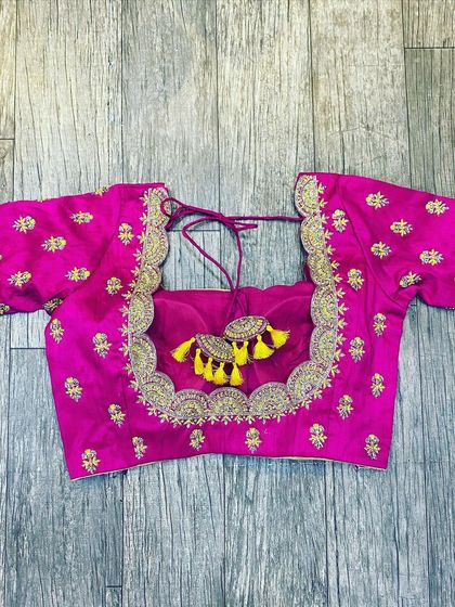 A pink blouse with gold butti work all over. The neckline has a heavy border, and the back features large, fun tassels in yellow.