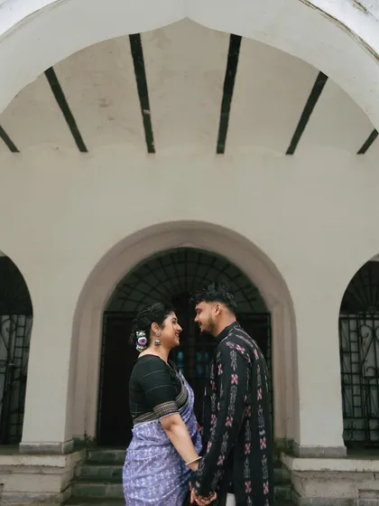 A symmetrical and intimate portrait under the arches of an old Sambalpuri building. The couple holds hands, their gaze locked, creating a powerful connection amidst the historic setting.