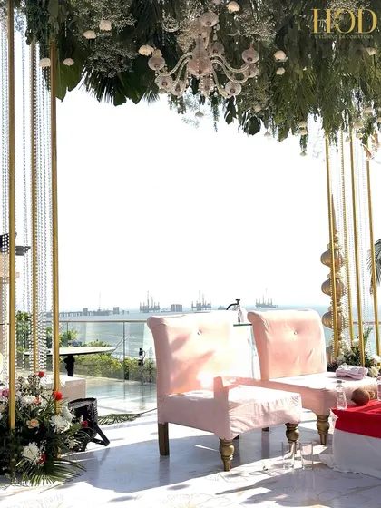 A detail shot from within the seaside mandap, looking out at the ocean, with the elegant pink chairs and floral canopy framing the view.