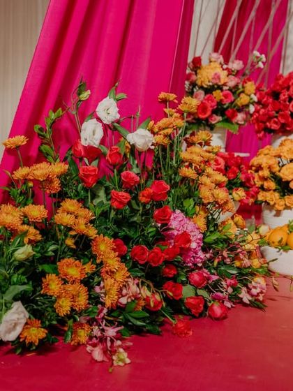 A floor-level floral installation with a rich palette of pink, orange, red, and white flowers, creating a lush, garden-like feel indoors.