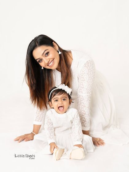 A playful moment between mother and daughter. The little one's happy expression is infectious in this bright and cheerful studio photo.