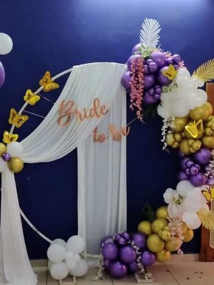 A different style of 'Bride to be' decoration, using a white circular frame, drapes, and a purple, gold, and white balloon garland.