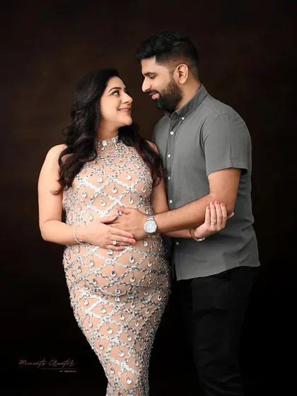 An elegant and intimate couple's portrait. The focus here is on the connection between the parents-to-be, captured with classic lighting against a rich, dark backdrop for a timeless feel.