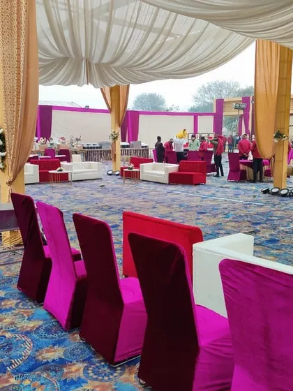 Inside the main wedding tent, I arrange comfortable lounge seating for guests. This setup includes white sofas with red and pink chairs, creating a relaxed yet elegant space for people to gather during the reception.