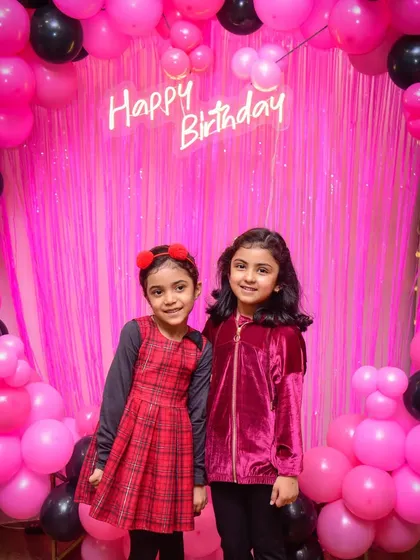 Two friends posing in front of the vibrant pink and black balloon backdrop.