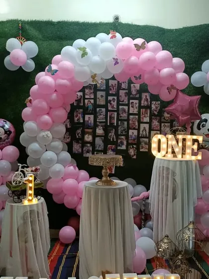 A pink and white balloon arch over a photo collage backdrop, creating a personalized centerpiece for a first birthday.