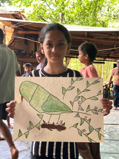 A young artist shows off her nature painting of a parrot, a wonderful souvenir from her time at the Ulavi camp.