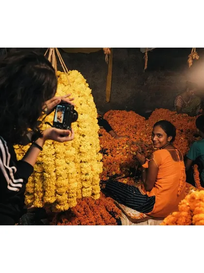 3:32am: In the early hours at the flower market, I capture another photographer taking a picture of a smiling female vendor. A meta-moment showing the intersection of life and documentation.