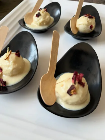 Our dessert menu features both modern and traditional Indian sweets. Here, we've presented a classic Rasmalai in elegant, single-serving spoons, garnished with delicate rose petals for a beautiful finish.