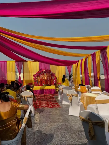 A full view of a rooftop Haldi or Mehendi setup, with guests seated under a canopy of pink and yellow drapes.