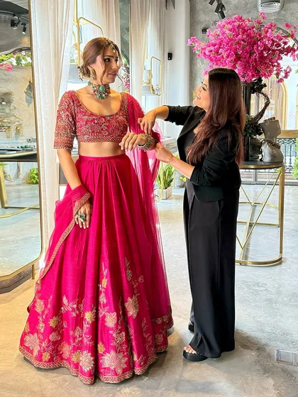 For her Mehendi, we styled makeup artist Sahiba Chona in a vibrant Rani pink lehenga. Here, we are in the final stages of accessorizing, ensuring every piece of jewelry complements the look perfectly.
