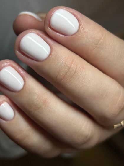 A crisp, clean white manicure on short, natural nails. The flawless application and high-gloss finish demonstrate the precision of our Russian manicure service.