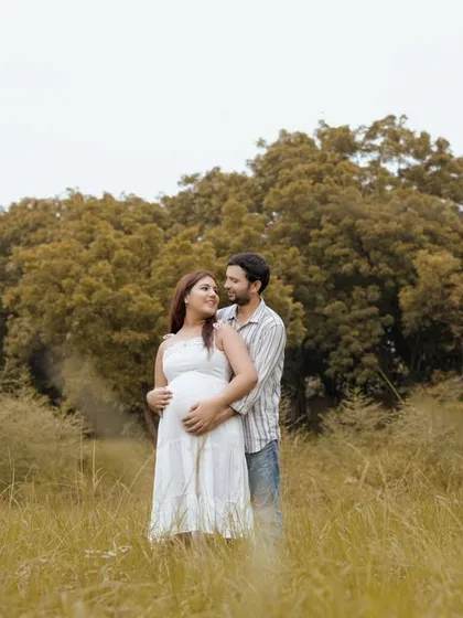 A classic couple's pose amidst the natural scenery. Their coordinated white outfits create a serene and timeless look for their outdoor pregnancy photoshoot.