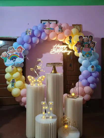 A pastel rainbow Cocomelon theme built around a circular ring backdrop. This decoration includes character cutouts placed along the balloon arch and a central neon 'Happy Birthday' sign, perfect for a toddler's party.