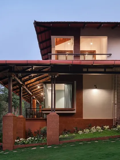 A closer view of the Dream Coffee Estate's layered facade, showing the interplay between the laterite base, the open veranda with its exposed timber structure, and the upper-level living spaces. The design creates multiple areas for enjoying the outdoors.