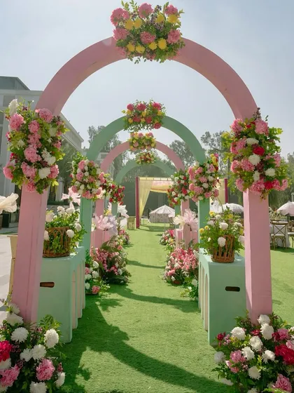 A beautiful floral entranceway for a pastel Haldi, with arches in alternating shades of pink and sage green, all adorned with fresh, colorful flower arrangements.