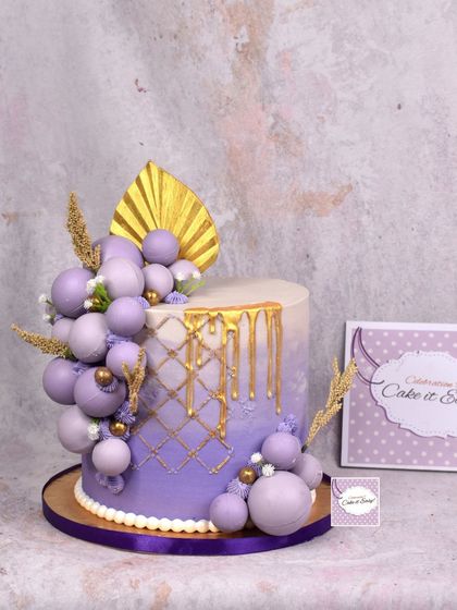 A modern and elegant purple ombre cake with a gold drip and chocolate sphere clusters.