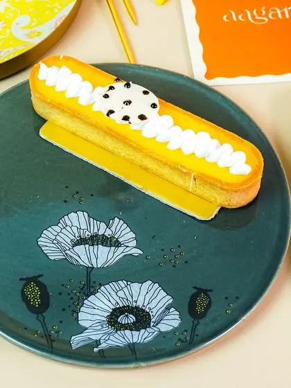 An eclair served on a beautiful hand-painted plate with a floral design, highlighting the product's artistic quality.