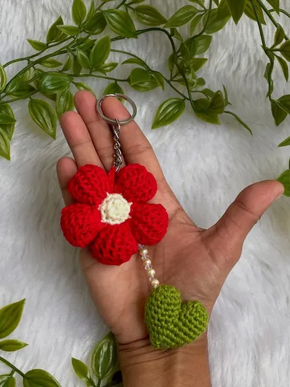 A pretty red flower keychain made with a special Tunisian crochet technique. The little green heart and pearl details make it extra special.