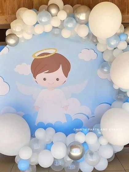An elegant balloon decoration for a baptism. The backdrop features a cartoon angel, framed by a soft blue, white, and silver balloon garland.