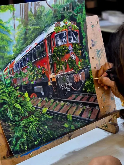 A student works on her detailed train painting. The wooden easel and studio background give a sense of our creative environment.