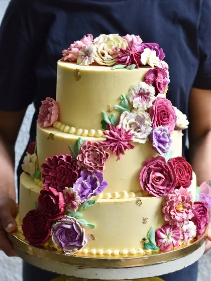 This three-tiered wedding cake is a celebration of colour and texture, covered in a cascade of hand-piped buttercream flowers. We don't use fondant, so every single petal is as delicious as it is beautiful, perfect for a grand wedding celebration.
