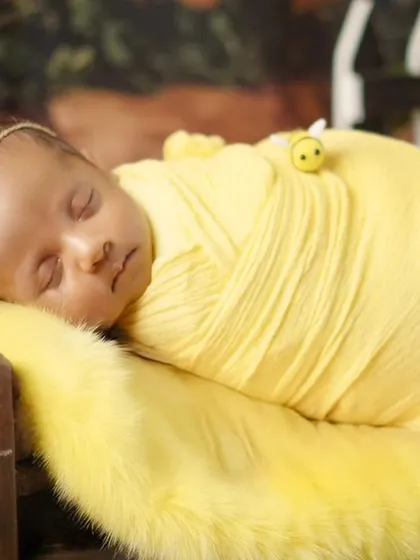 A close-up of the sleeping honey bee newborn, showcasing the delicate floral headband and the cozy yellow swaddle.