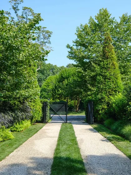 A creative driveway design using a combination of gravel and twin strips of turf. This approach softens the hardscape and is framed by lush, layered plantings and mature trees for a grand entrance.