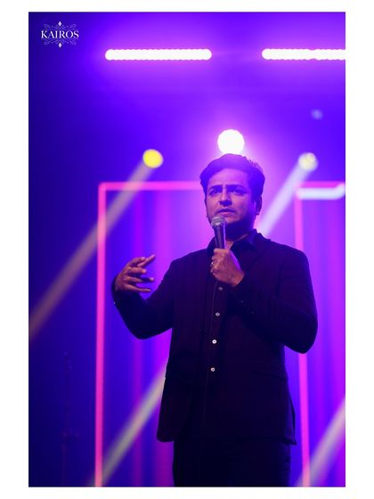A performer speaking into a microphone under purple stage lights, capturing the mood and atmosphere of the event.
