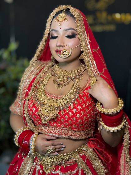 This bride looks radiant in her red and gold bridal attire. The makeup is focused on creating a glowing, flawless base with a bold winged eyeliner and heavy jewelry.