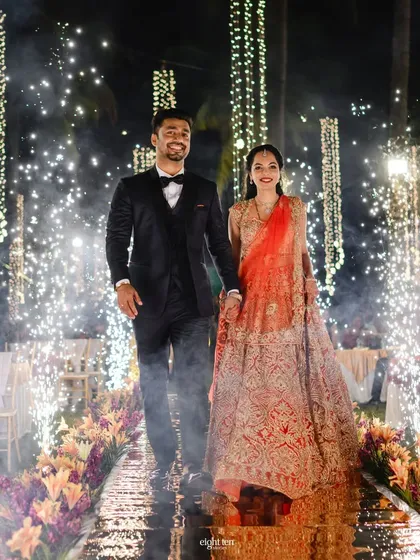 The couple's grand reception entrance through an aisle of sparklers. The path is lined with flowers and fairy lights, leading them into a night of celebration.