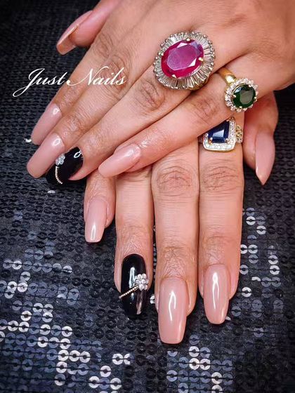 An elegant set of long, square-shaped nude nails with black accent nails featuring delicate rhinestone bow details.