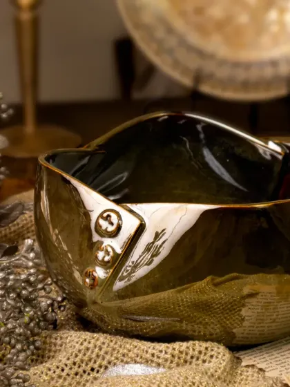 Another angle of the stunning metallic bowl, this time styled on a rustic surface with newspaper and shimmering props. The lighting catches the unique contours and glossy finish of the ceramic.