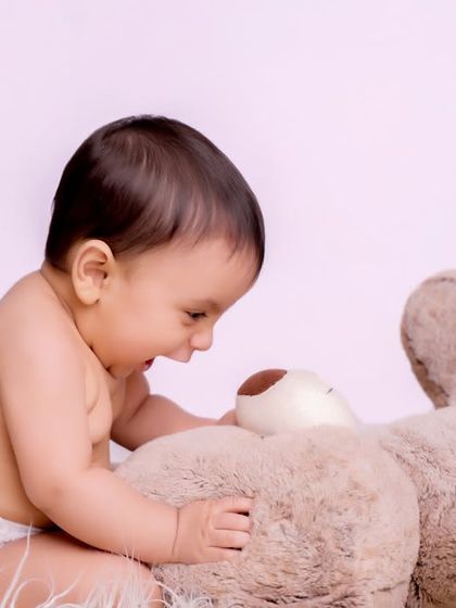 A baby shares a happy moment with a fluffy teddy bear. We use classic props to create sweet and innocent portraits that focus on your child's connection with their favorite toys.