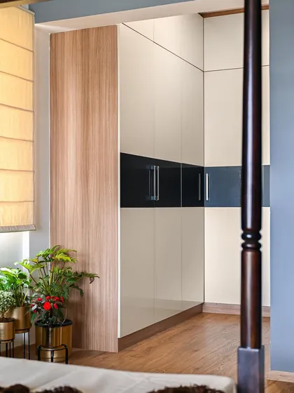 This L-shaped wardrobe features a seamless acrylic finish in off-white and black. The design provides ample storage while maintaining a sleek and modern look, perfectly integrated into the corner of the bedroom.