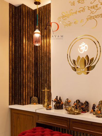A close-up of a modern pooja space with a marble countertop, fluted wood paneling, and a wall adorned with a golden Om and lotus symbol.