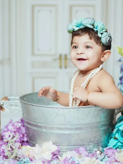 A joyful baby enjoying a milk bath session. The setup is adorned with blue and purple flowers for a beautiful, soft look.