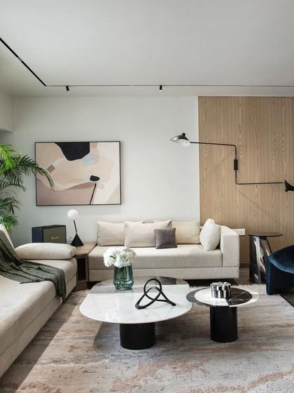 A living room featured by FOAID India. The space combines a neutral sofa with a bold blue armchair and a mix of marble and wood tables, showcasing a sophisticated blend of colors and materials.
