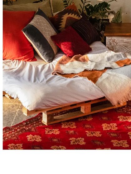 A cozy seating area with a bed made from wooden pallets, layered with colorful textiles and a traditional red rug.