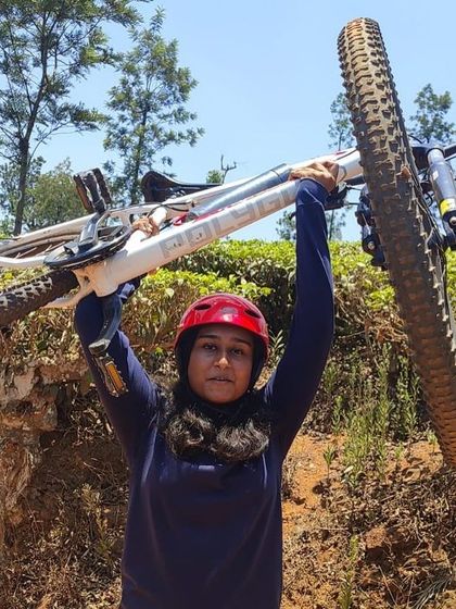 A participant proudly holds her bike aloft, celebrating her accomplishment on the trails of Barapole.