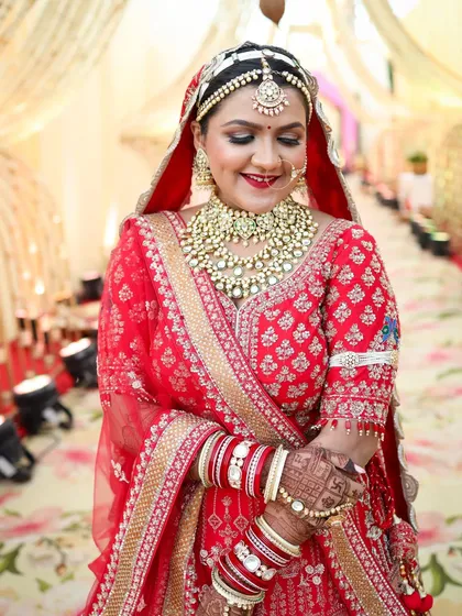 A beautiful, happy moment captured. The bride's smile shows her confidence, with her makeup looking fresh and radiant. The bold red lip and defined eyes are key elements of this traditional Indian bridal look.