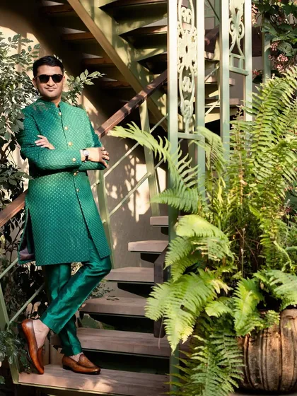 The groom looking sharp in his custom-designed bottle green sherwani. The self-embroidered fabric and gold buttons add a regal touch, while the setting among the ferns feels perfectly Goan.