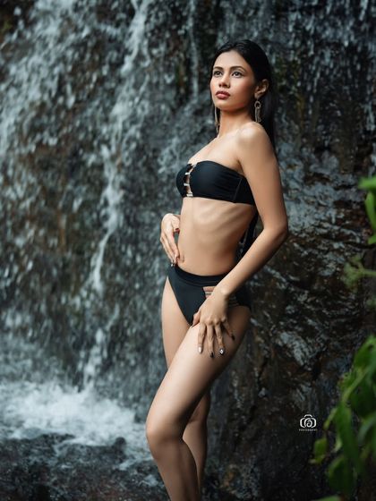 A full-body shot of the model standing in front of the waterfall. This image captures the scale of the natural scenery and the model's confident presence within it.