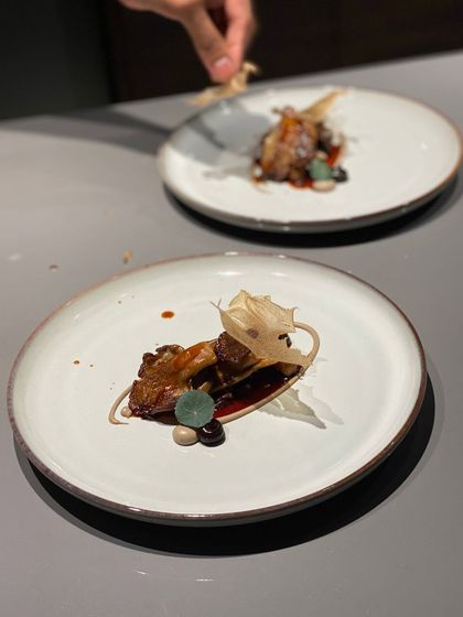 The final touch being added to a complex appetizer. This dish combines earthy mushrooms with a rich sauce and a delicate, crispy tuile.
