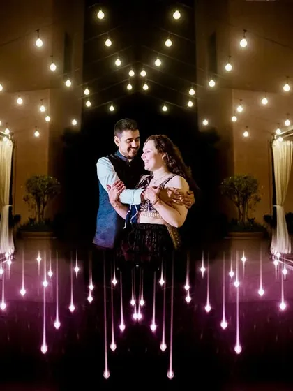 A symmetrical and creative portrait using reflections and light. The couple stands amidst a "sky full of stars" created by string lights, resulting in a magical and visually stunning image.