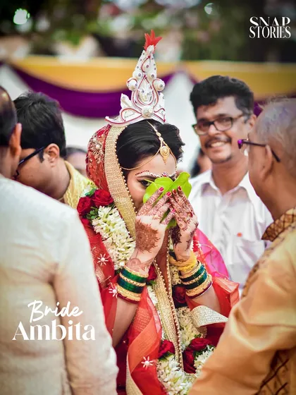 A Bengali bride participates in the Shubho Drishti ritual, hiding her face behind betel leaves. We have experience with diverse Indian wedding traditions and capture them authentically.