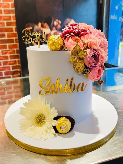 Elegance in its simplest form. This tall, single-tier birthday cake is adorned with a cascade of fresh flowers, Ferrero Rocher chocolates, and a personalized gold acrylic nameplate, making it a sophisticated choice for any adult celebration.