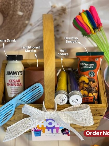 Our festive Holi hamper, packed in a rustic wooden basket. It includes Kesar Thandai, organic Holi colors, a healthy snack mix, and quirky glasses.